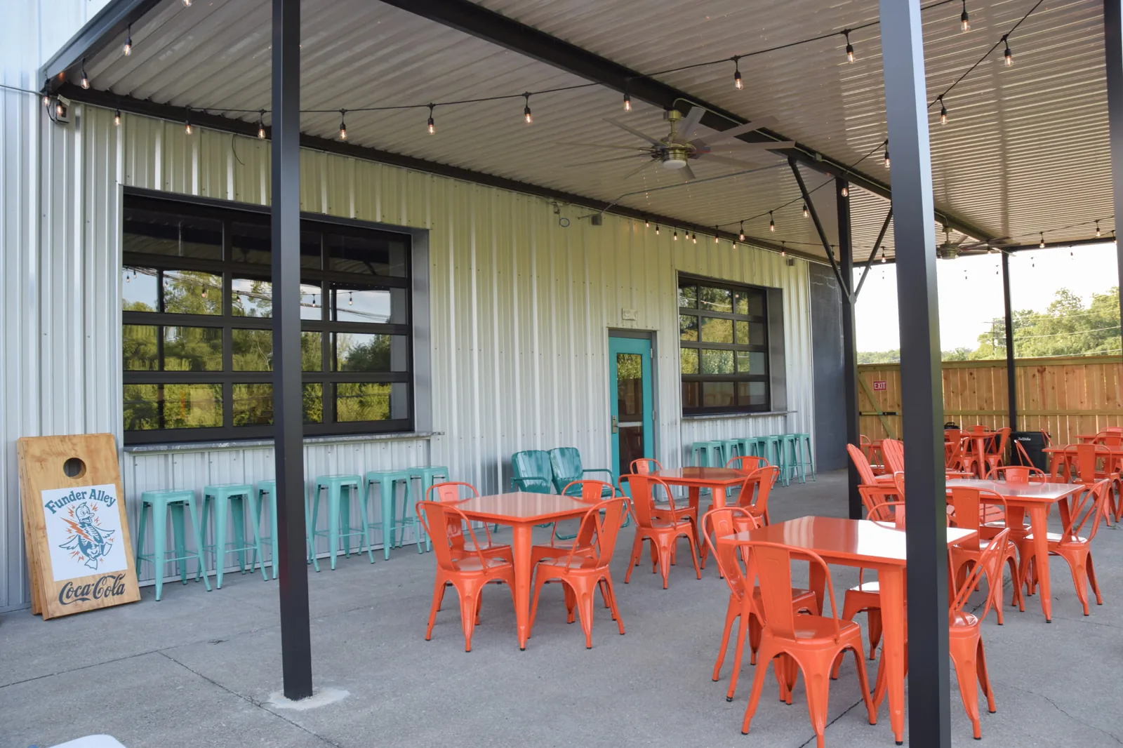 Funder Alley's covered outdoor patio with string lights, orange and teal tables, and a cornhole board