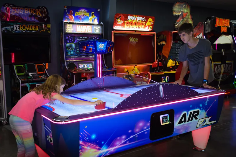 Two players facing off over a lit air hockey table in the arcade