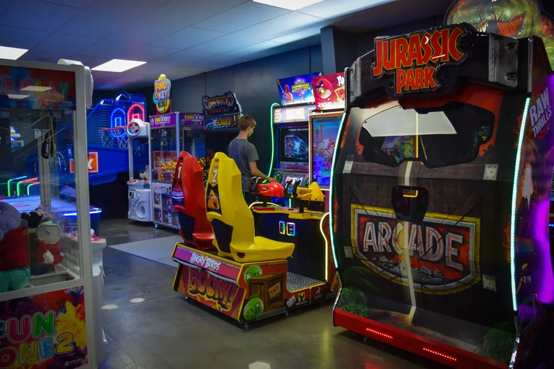 A row of arcade cabinets including claw machines and a motorbike racer