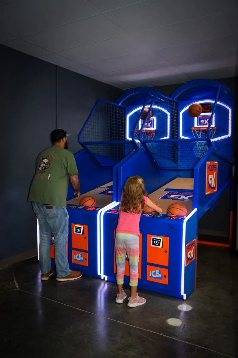 An adult and a child shooting baskets side by side on the arcade hoops game
