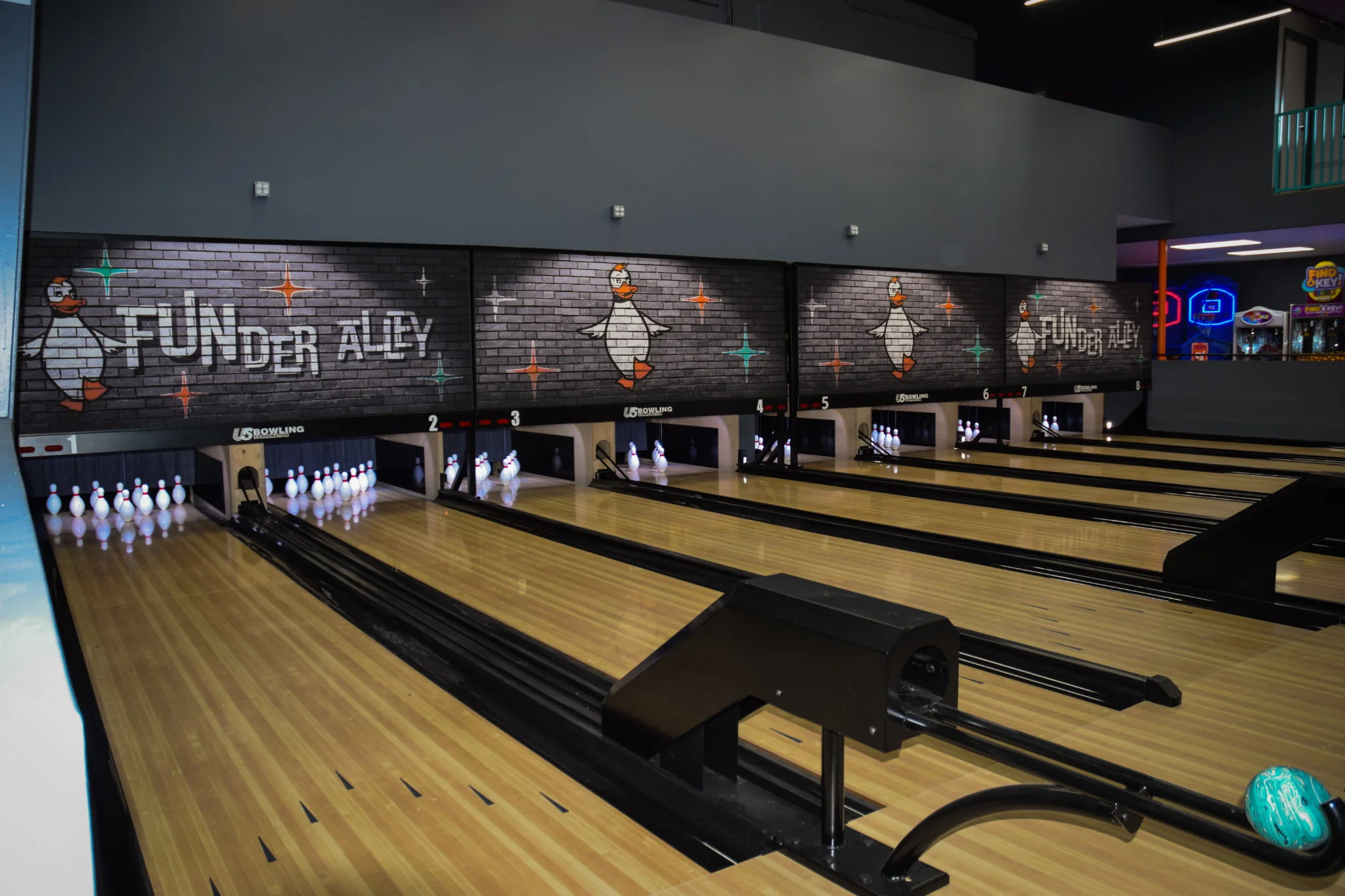 Funder Alley's eight duckpin lanes with full racks of pins and FUNder Alley duck murals above the pin decks